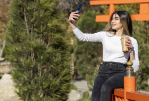 Mulher fazendo uma selfie segurando um copo de café, exemplo de registro estratégico para fazer marketing para cafeteria