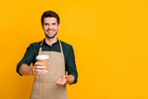 Homem de avental seguyrando copo de café de papel num fundo amarelo