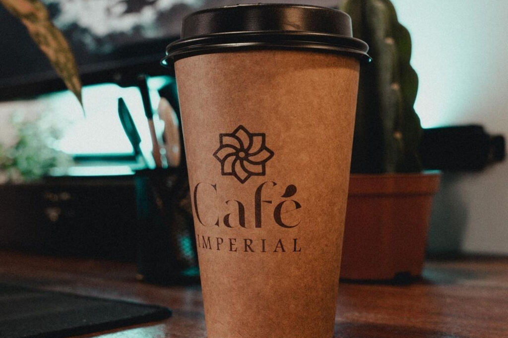 Copo de café de papel kraft com tampa personalizado usado para viagem e delivery em cima de uma mesa