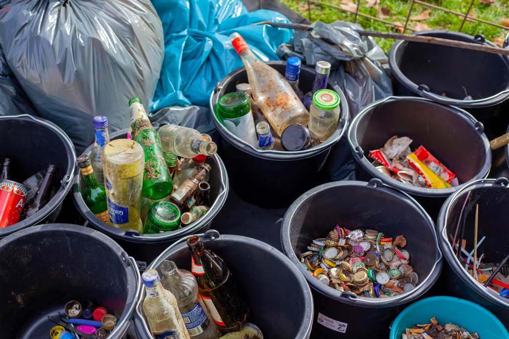 Sacos de lixo e cestos com resíduos recicláveis separados, como: garrafas e potes de vidro, tampinhas de alumínio, lacres de plástico, etc. Ilustrando a reciclagem no Brasil