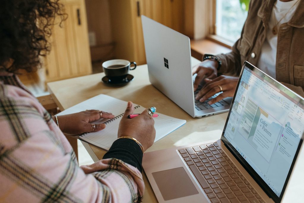 Duas mulheres fazendo planos de negócios, cada uma usando um notebook, e uma delas fazendo anotações num caderno. Representando como abrir uma sorveteria