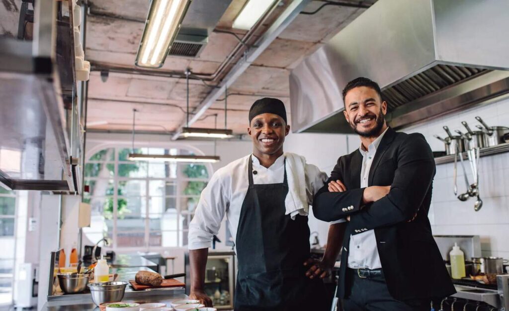 Dois homens sorrindo em uma cozinha de restaurante