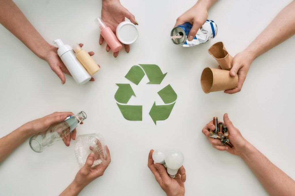 Símbolo da reciclagem com mãos em volta segurando materiais recicláveis