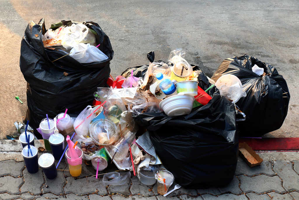 Embalagens de plástico e lixo dentro de três sacos pretos, representando o tempo de decomposição dos materiais