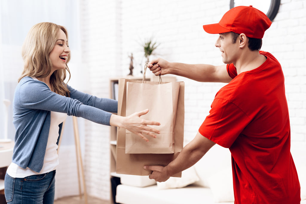 Entregador fazendo delivery sustentável, entregando sacolas de papel para uma compradora sorridente