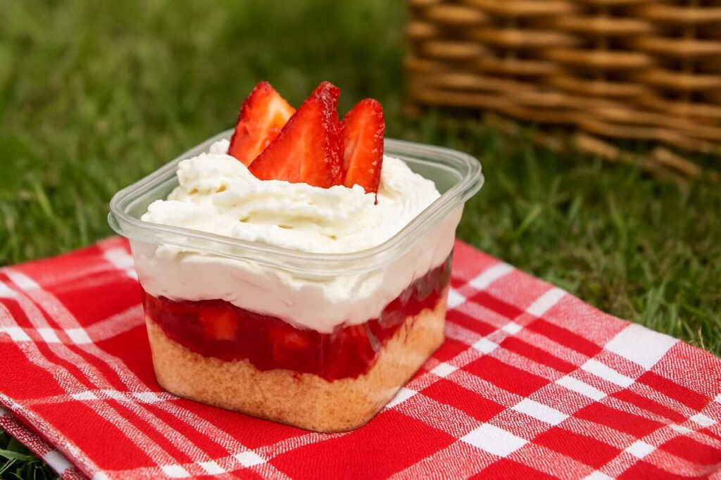 Bolo de pote de morango com camadas de bolo, geleia e chantilly, decorado com morangos frescos sobre toalha xadrez vermelha.