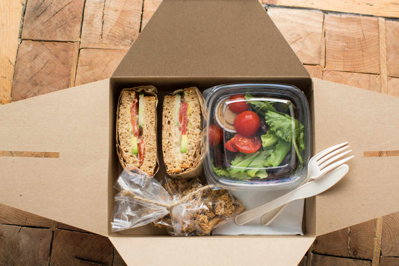 Caixa com dois sanduíches, biscoitos embalados e uma marmita com salada dentro.