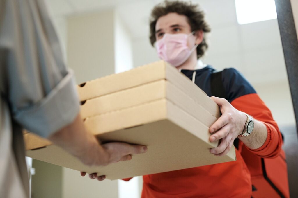 Homem com máscara segurando três caixas de pizza