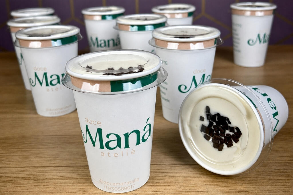 Copos para delivery personalizados com identidade visual de doceria e tampa transparente em cima de uma mesa de madeira