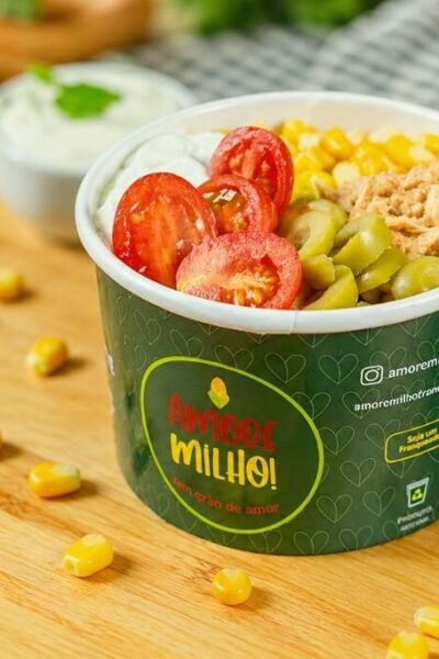 Embalagem para petiscos de papel personalizada com milho, tomate, azeitonas e frango desfiado dentro em cima de uma mesa de madeira
