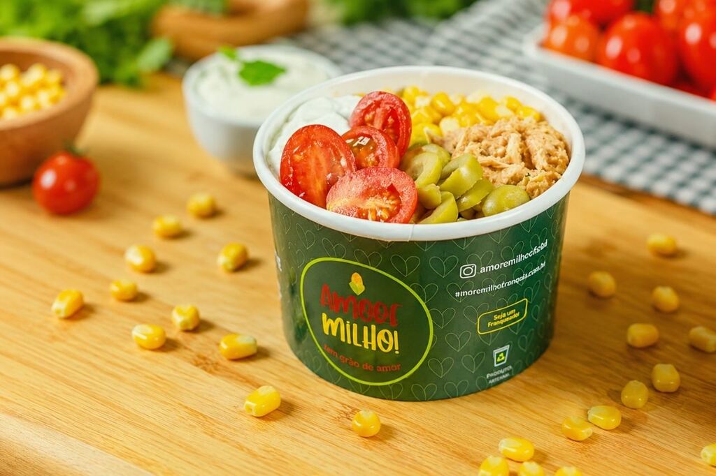 Embalagem para petiscos de papel personalizada com milho, tomate, azeitonas e frango desfiado dentro em cima de uma mesa de madeira